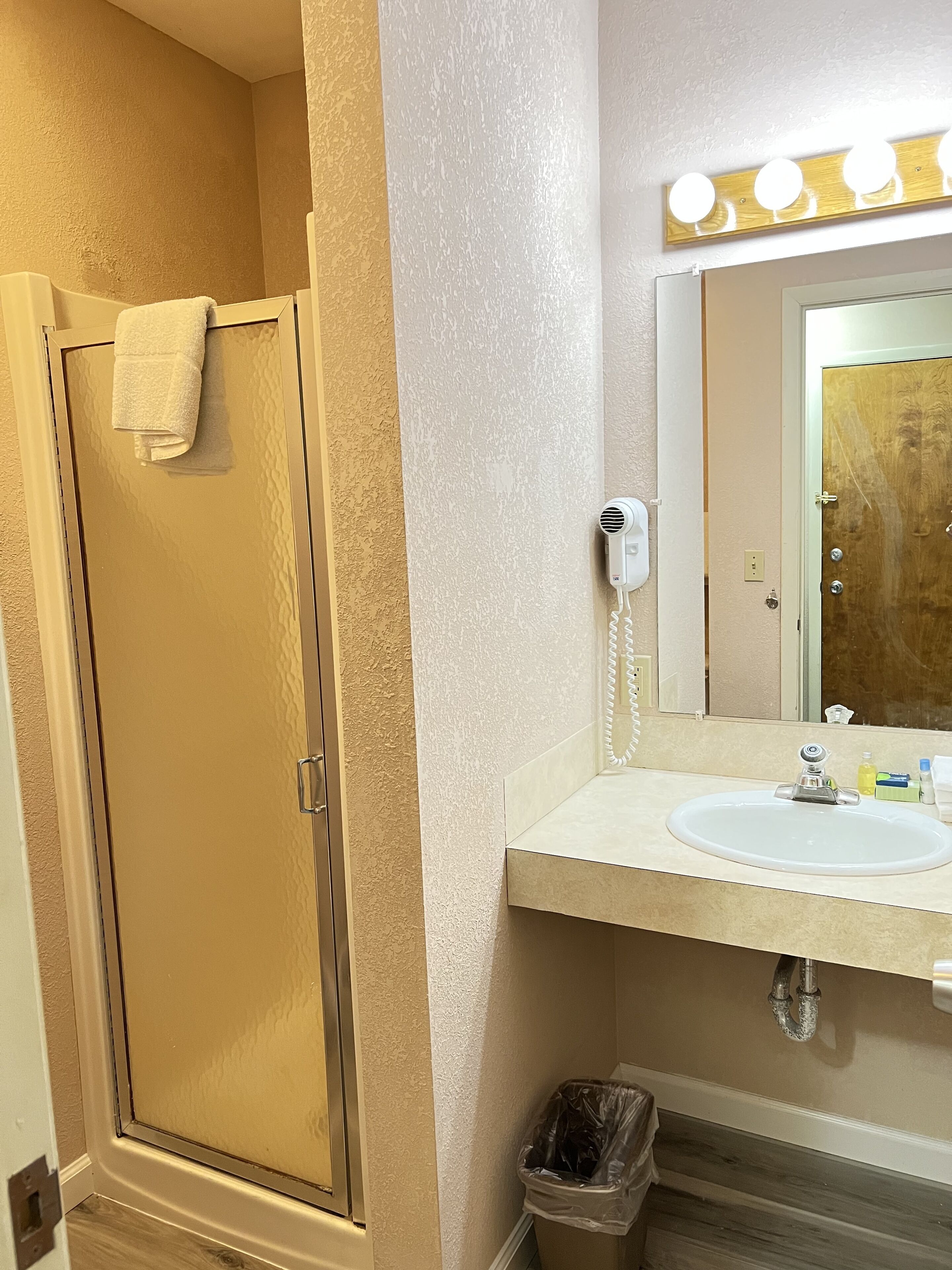 Une salle de bain avec une douche, un meuble-lavabo et un miroir avec des lumières au-dessus.