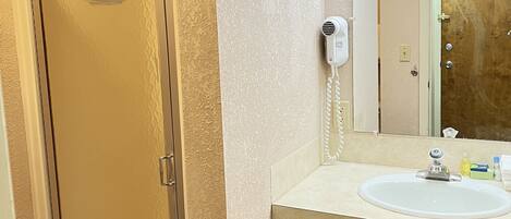A bathroom with a shower, a vanity with a sink, and a mirror with lights above it.