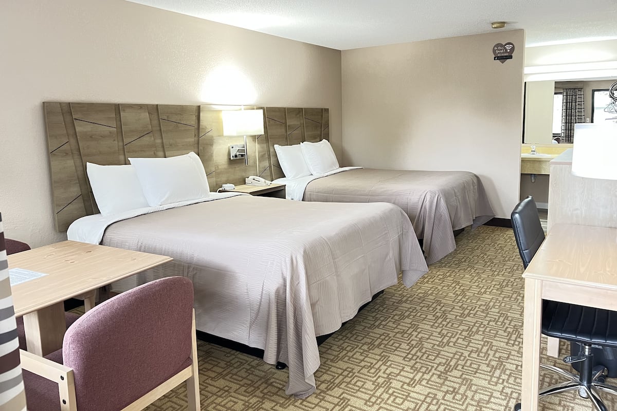 A hotel room with two beds, a desk, a chair, a lamp, and a mirror.