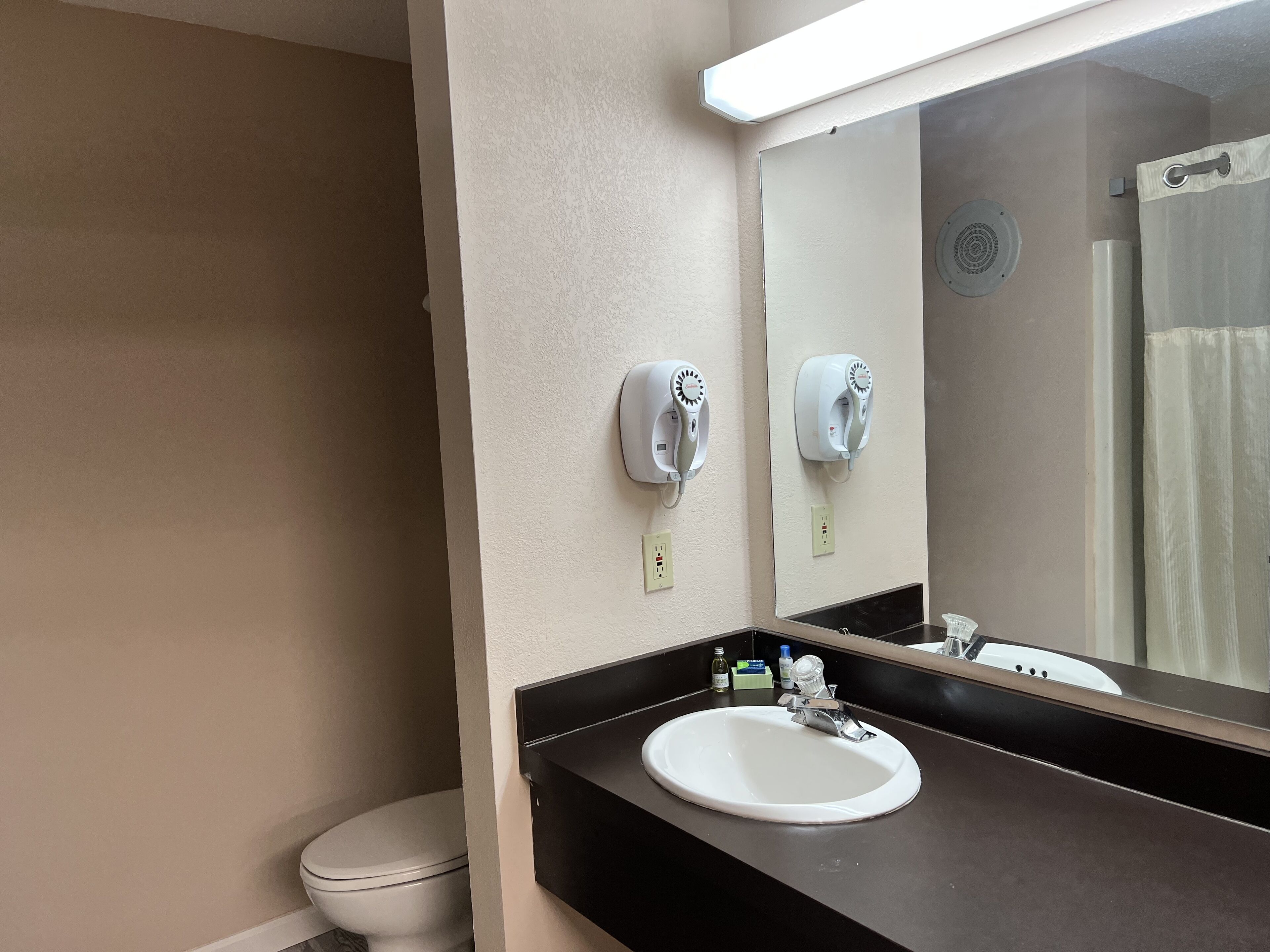 Une salle de bain avec un lavabo blanc, un miroir et deux sèche-mains fixés au mur.
