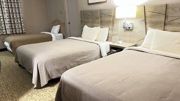 A hotel room with two beds, a wooden headboard, a nightstand, a lamp, and a painting on the wall.