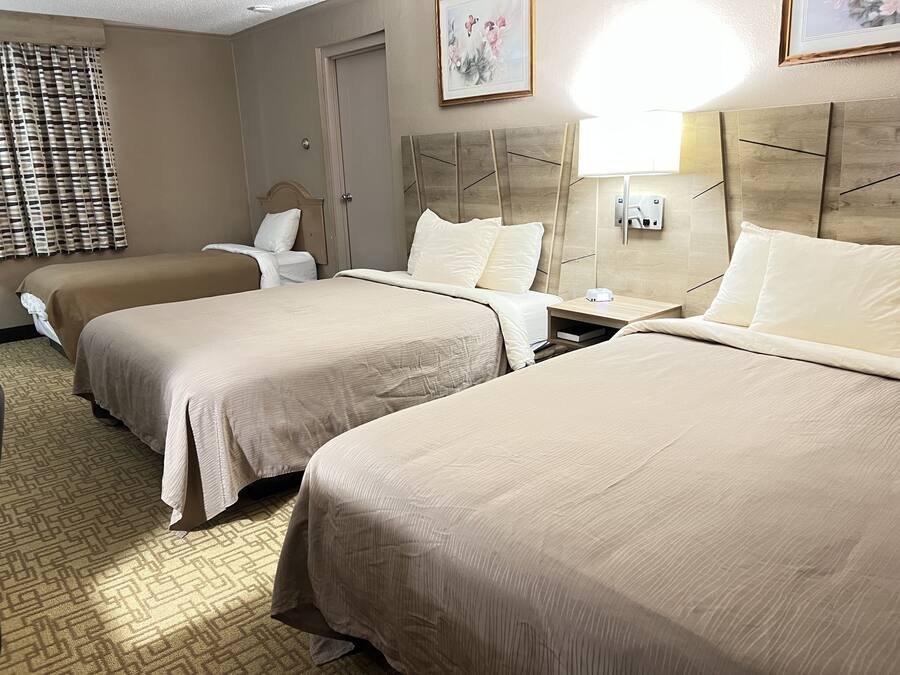A hotel room with two beds, a wooden headboard, a nightstand, a lamp, and a painting on the wall.