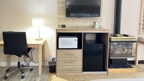 A hotel room with a desk, chair, TV, microwave, refrigerator, and a wood-burning stove. - Viking Arms Inn (Ludington)