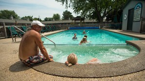 A swimming pool with a stone edge, lounge chairs, and a small building with a sign. - Viking Arms Inn (Ludington)