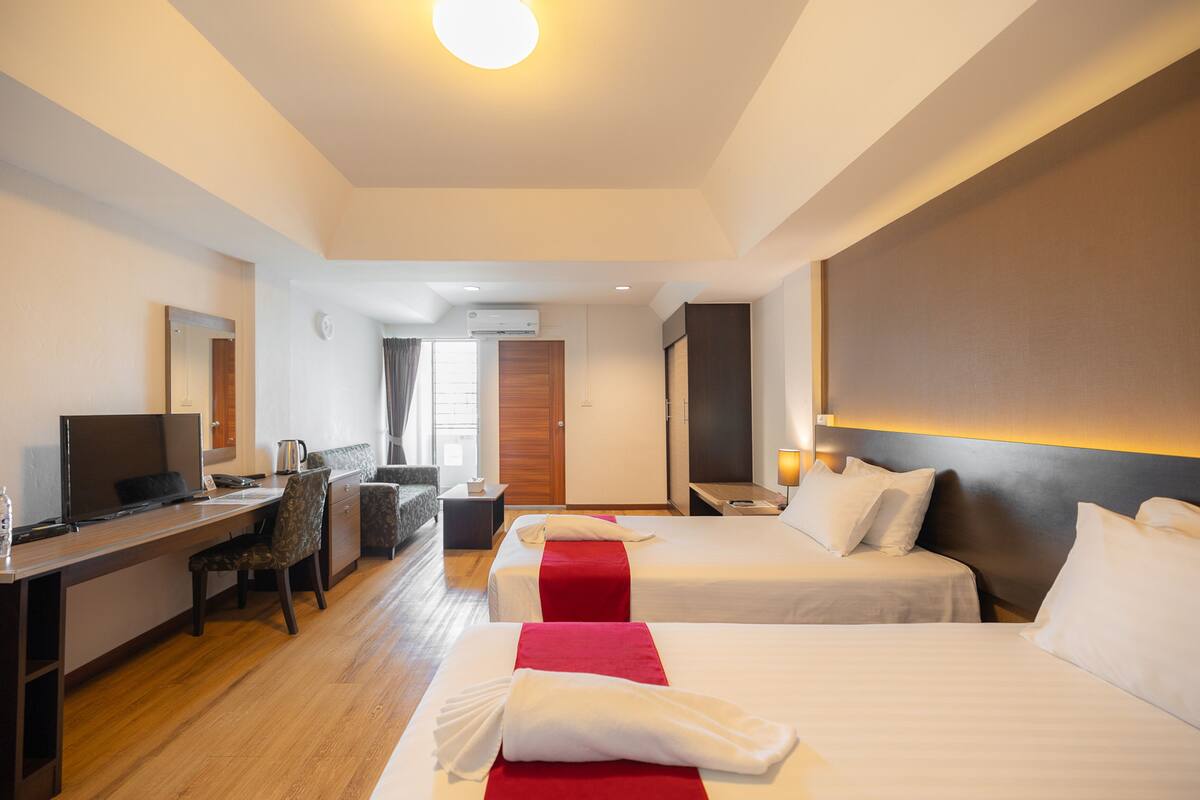 Hotellihuone, jossa on kaksi sänkyä, työpöytä tuolilla, televisio ja pieni pöytä lampun kanssa.