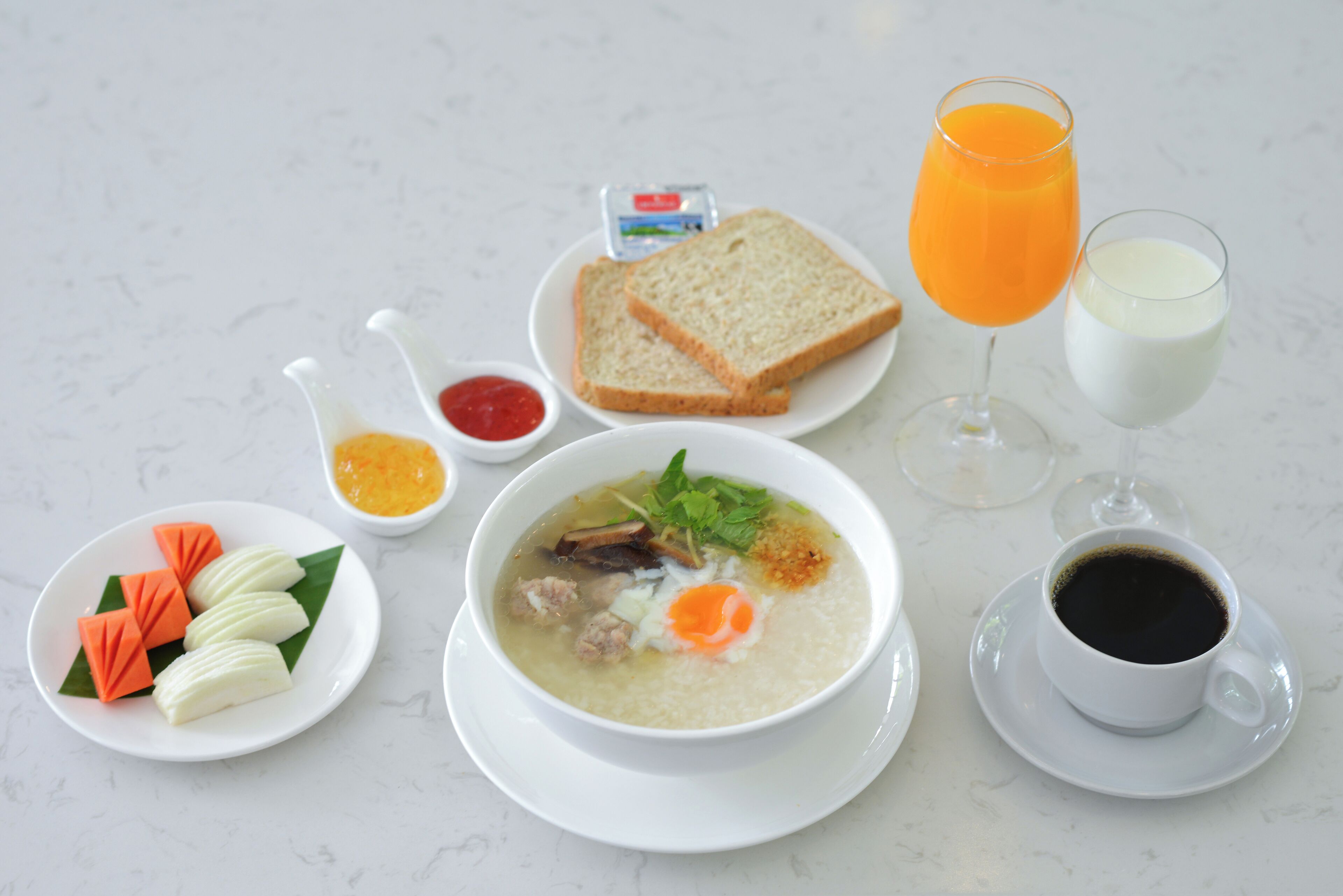 A table with a bowl of soup, slices of bread, a glass of orange juice, a cup of coffee, and a plate with dumplings and vegetables.