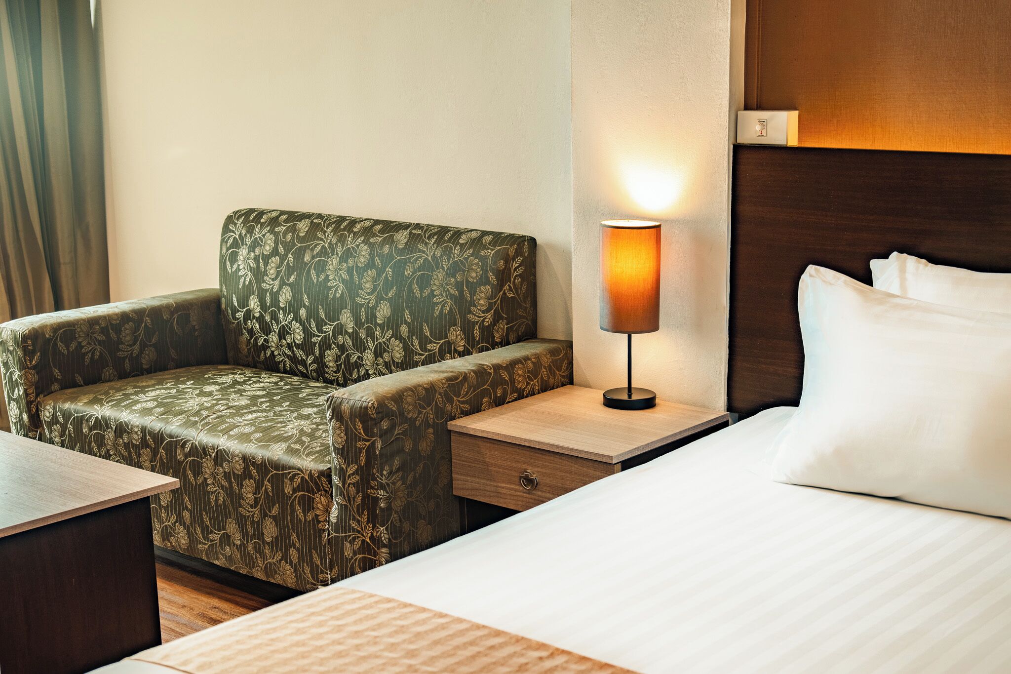 Habitación de hotel con cama, mesita de noche, lámpara, silla y mesa de madera.