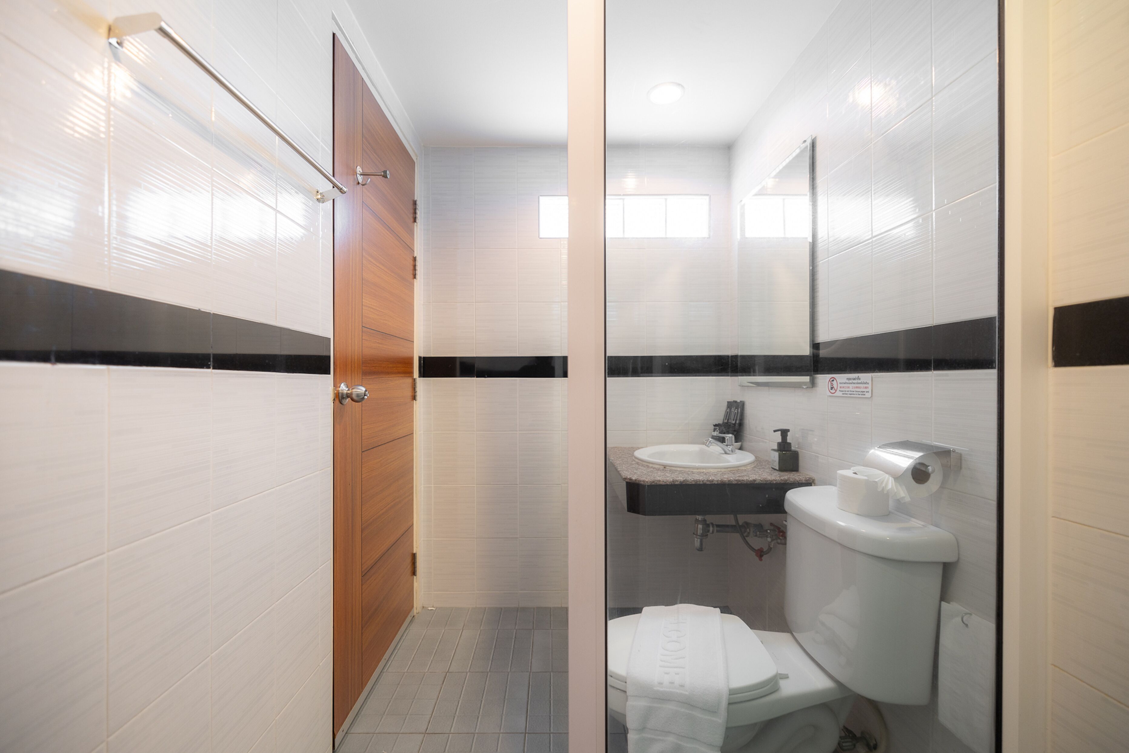 A modern bathroom with a wooden door, white tiled walls, a sink, and a toilet.
