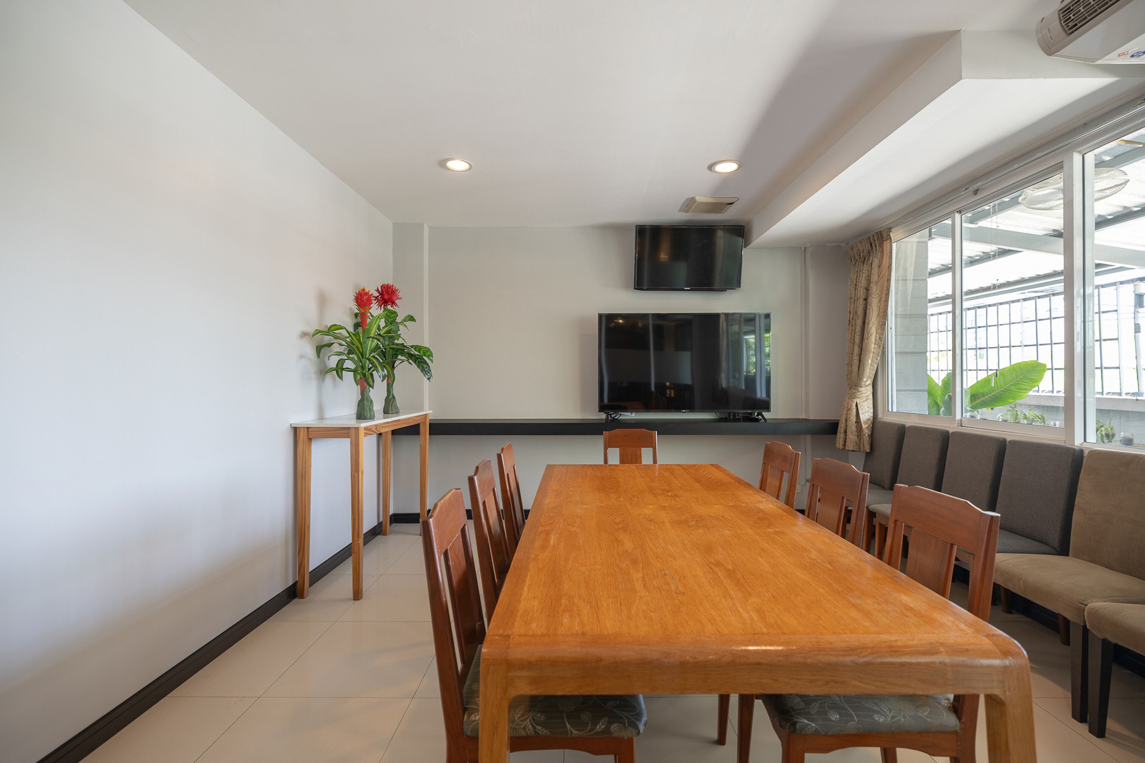 Un comedor con una mesa y sillas de madera, un televisor montado en la pared y un ventanal con vistas a la vegetación.