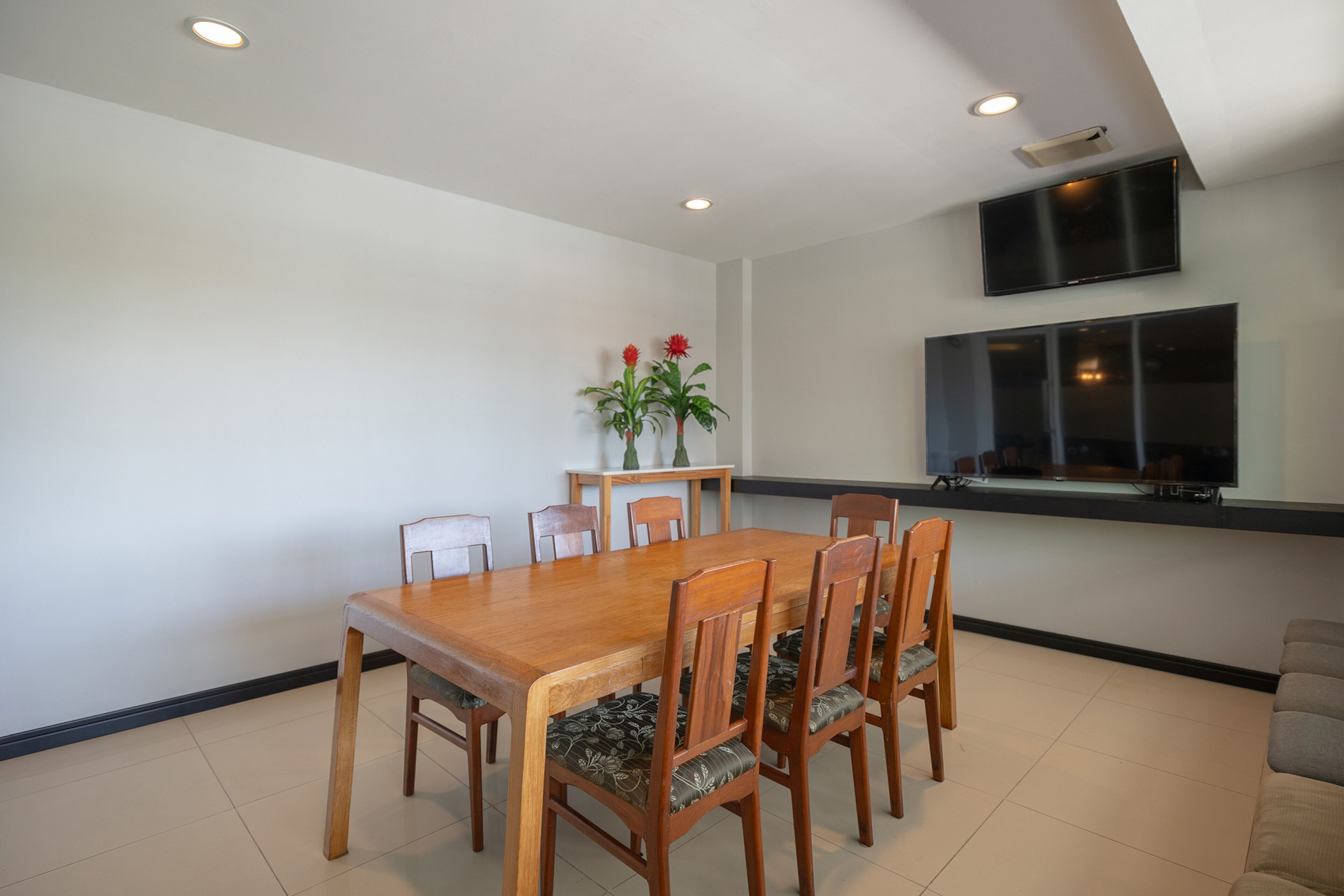 A dining area with a wooden table and chairs, a small plant, and a flat-screen TV mounted on the wall.