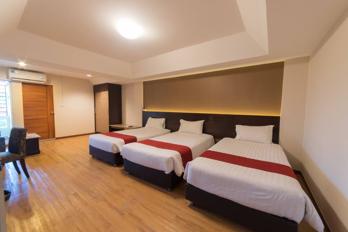 Hotellihuone, jossa on kolme sänkyä, puulattia ja moderni sisustus.