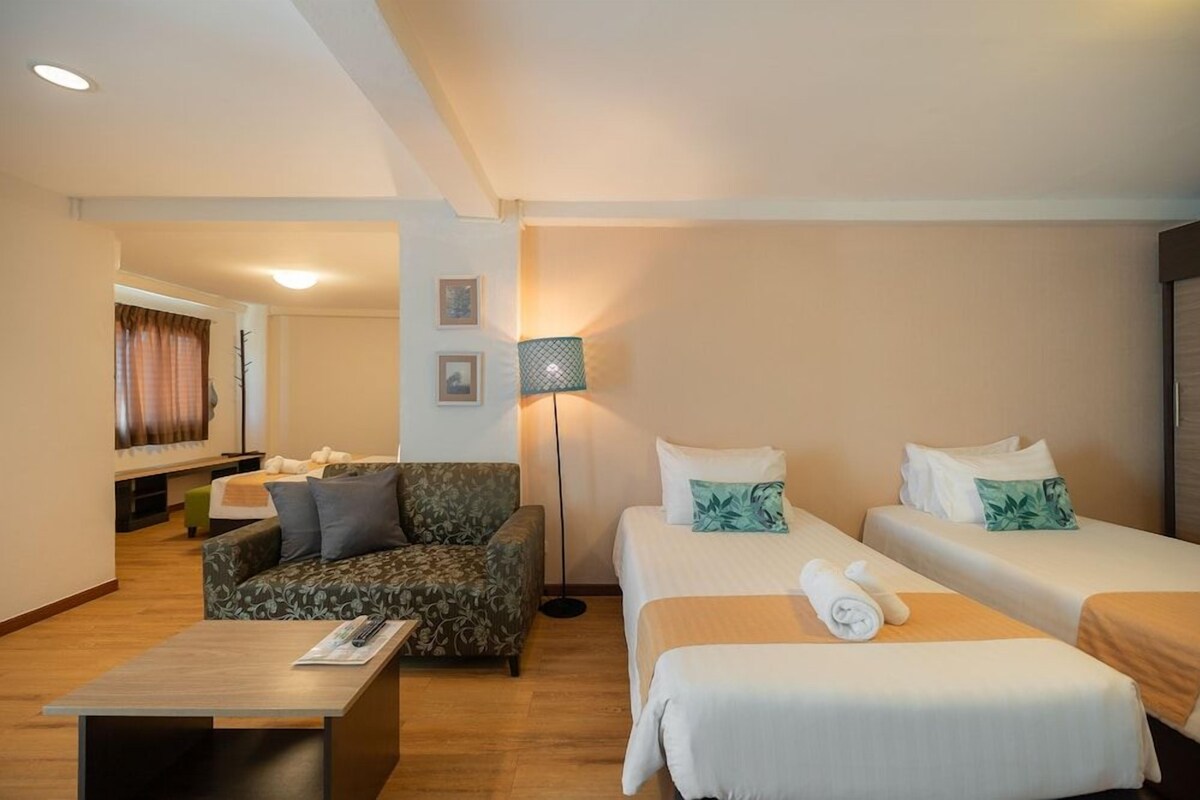 Una habitación de hotel con sofá, dos camas, una lámpara y una mesita.