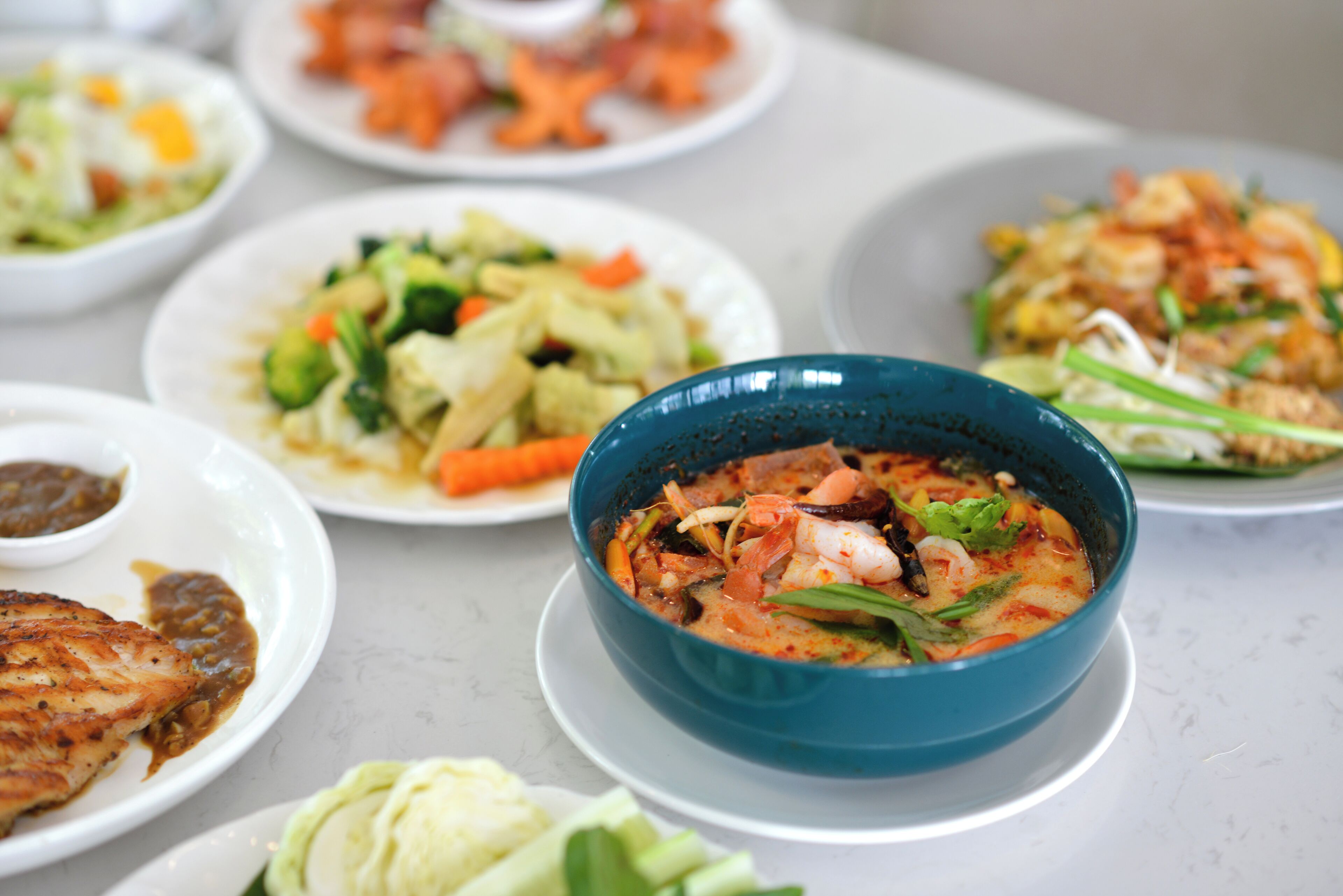 A variety of dishes on a table, including a bowl of soup with shrimp and vegetables, and other plates with different meals.
