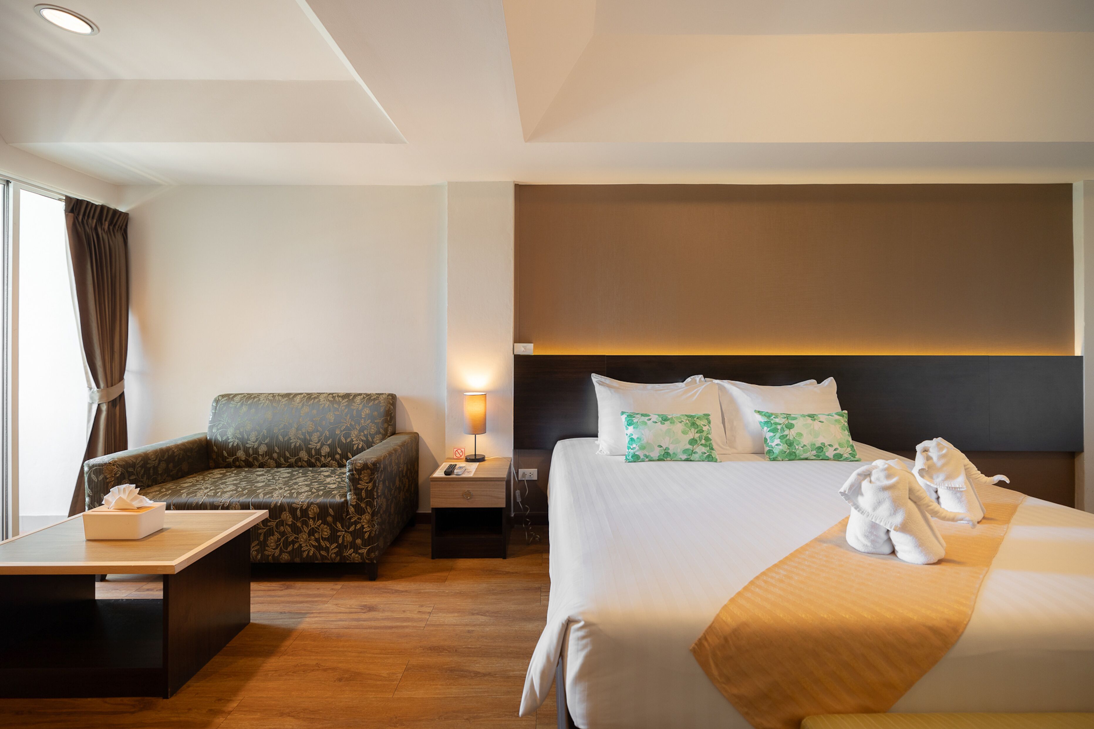 Une chambre d’hôtel avec un lit, un canapé, une table de chevet, une lampe et une fenêtre avec des rideaux.