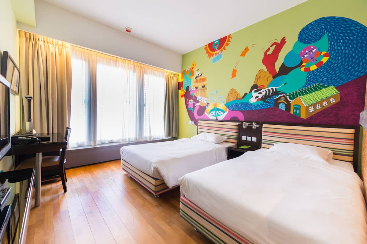 A hotel room with two beds, a desk, and a large colorful mural on the wall.
