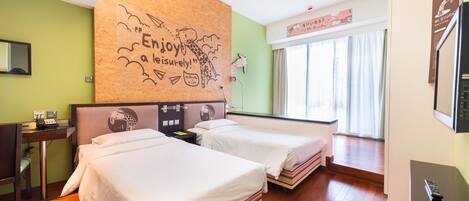 A hotel room with two beds, a desk, a mirror, and a giraffe-themed wall.
