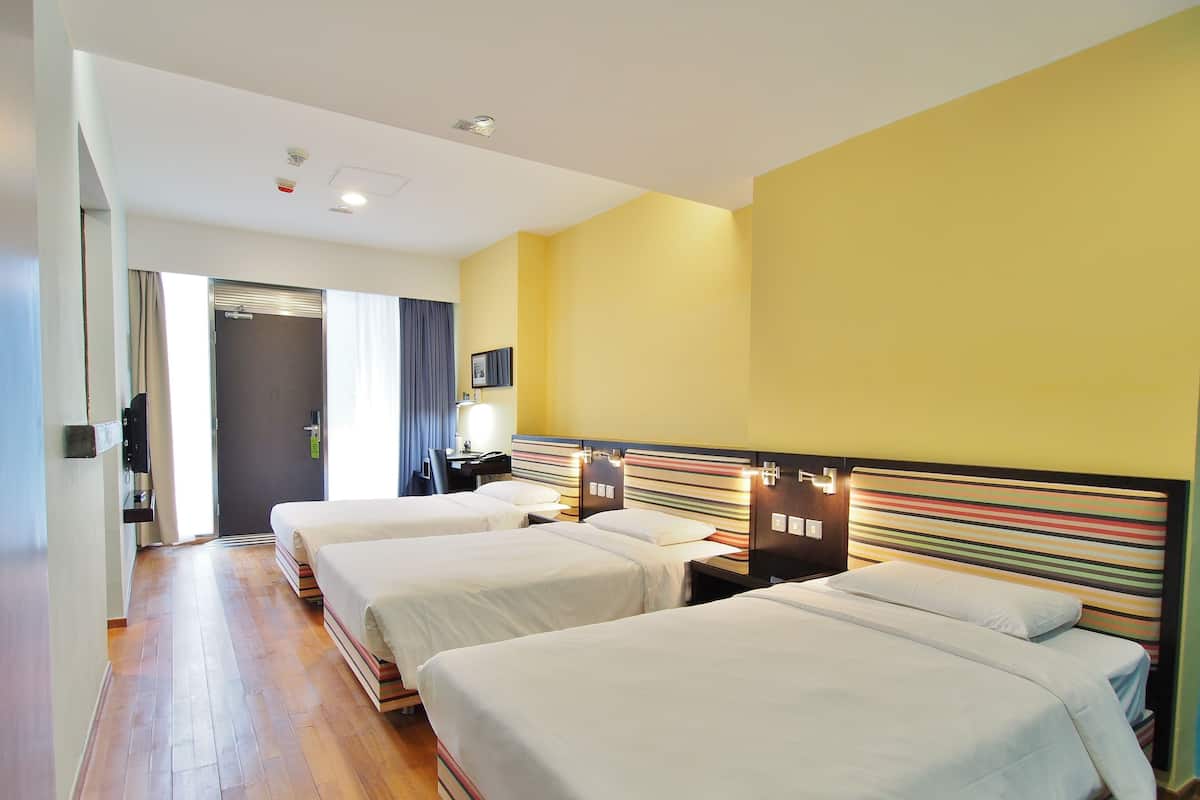 A hotel room with three single beds, a desk, and a chair.