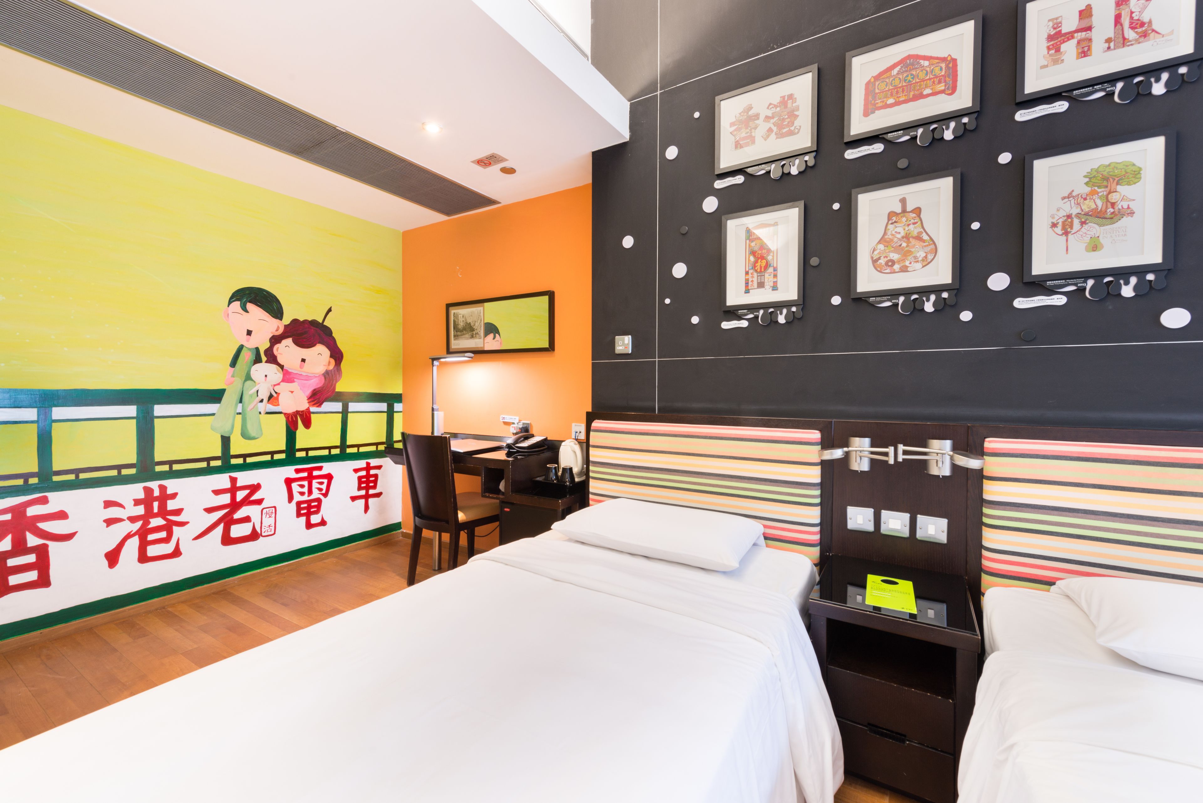A hotel room with a bed, desk, chair, and artwork on the walls.