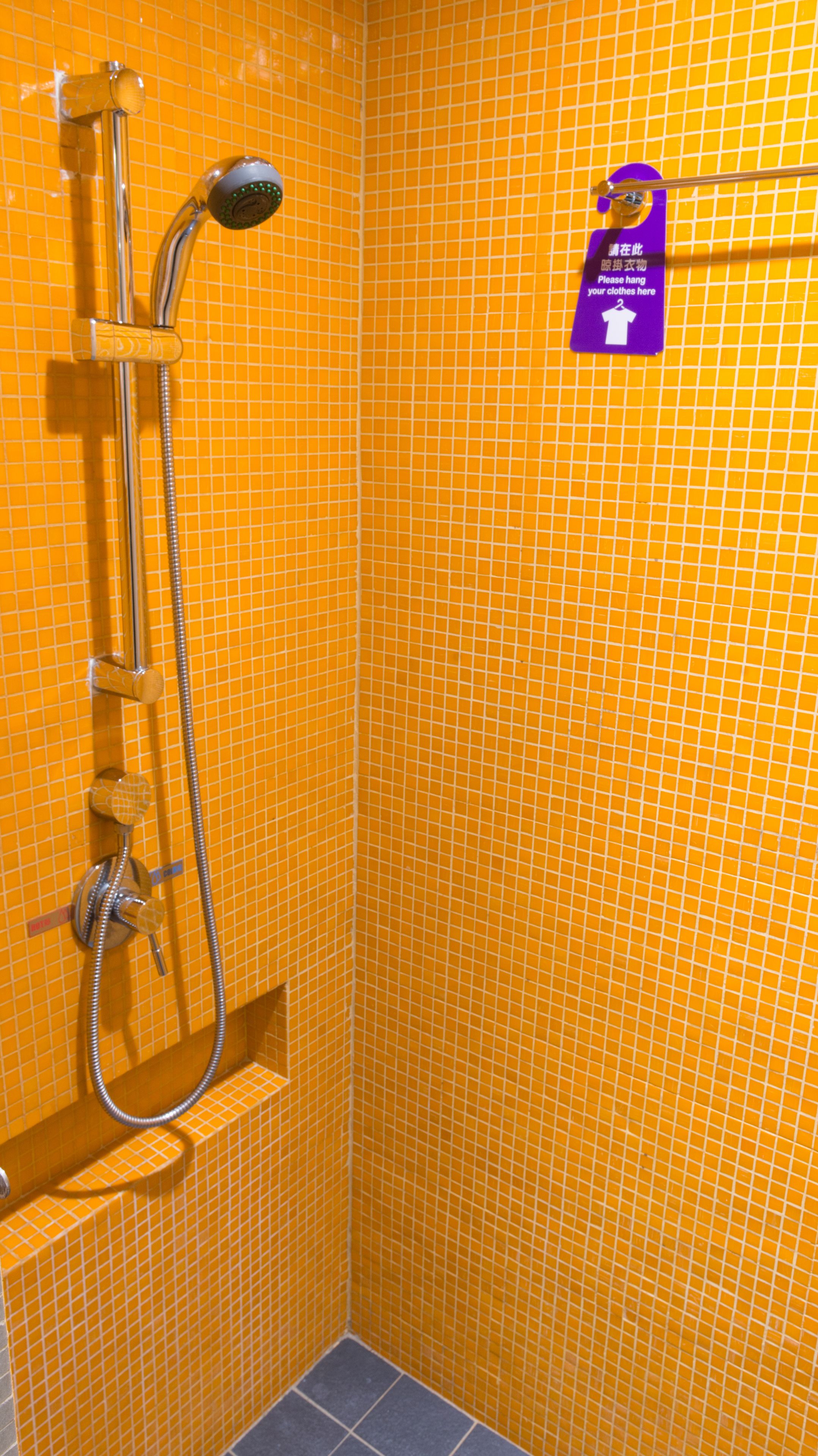 A shower area with a hand shower and a towel rack with a sign.