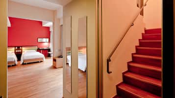 A hotel room with a wooden floor, a red wall, and a staircase with a metal handrail.