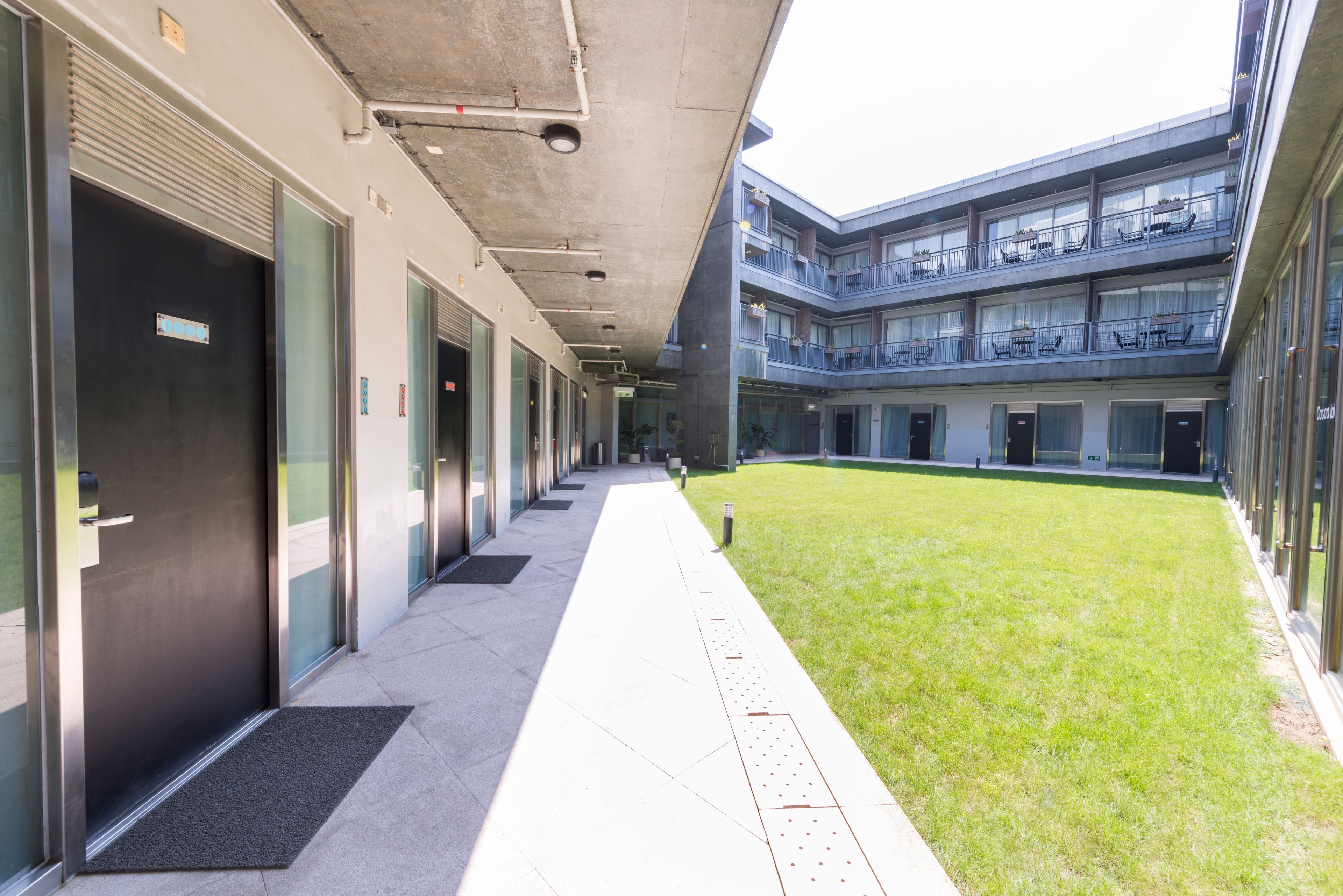 A modern building with a covered walkway, multiple floors, and a grassy courtyard.