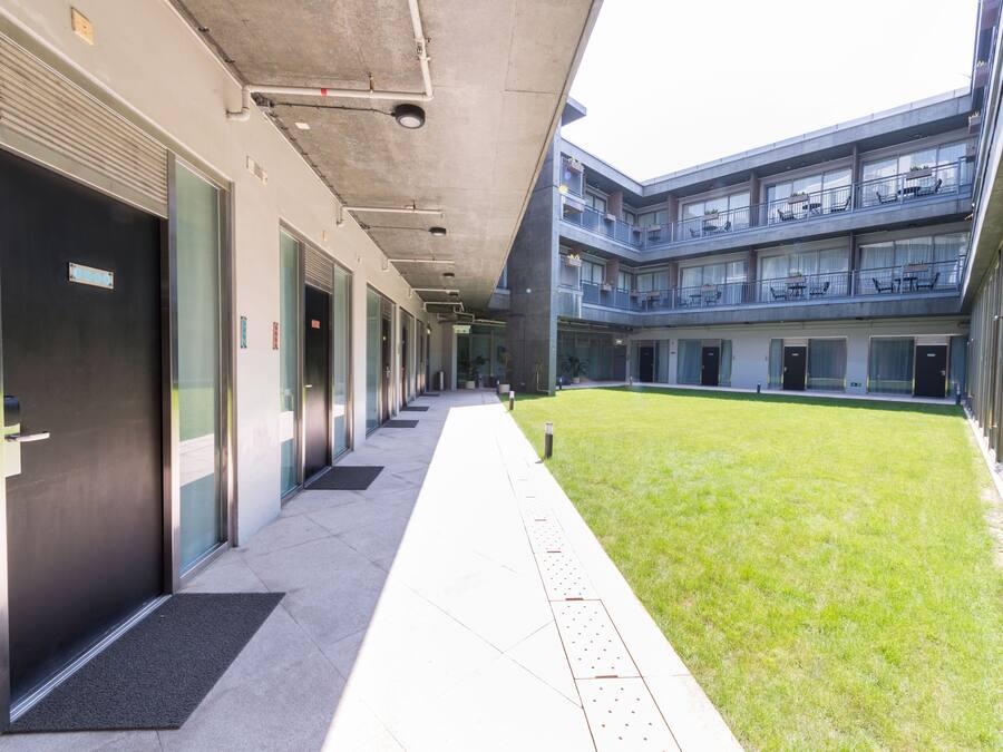 A modern building with a covered walkway, multiple floors, and a grassy courtyard.
