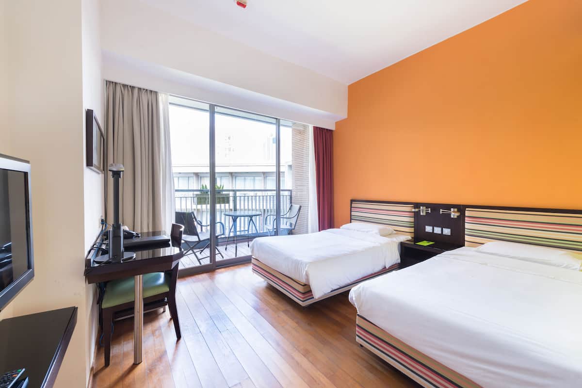 A hotel room with two beds, a desk with a chair, a TV, and a balcony with a table and chairs.