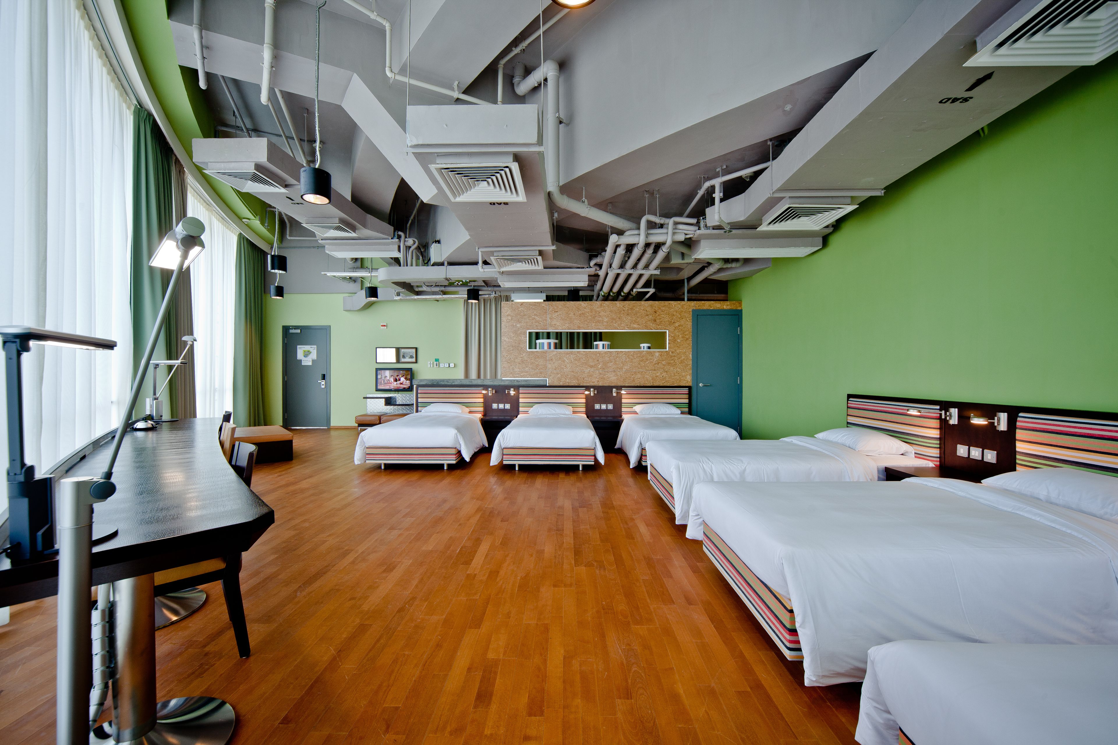 A hotel room with four single beds, a desk, and a chair.