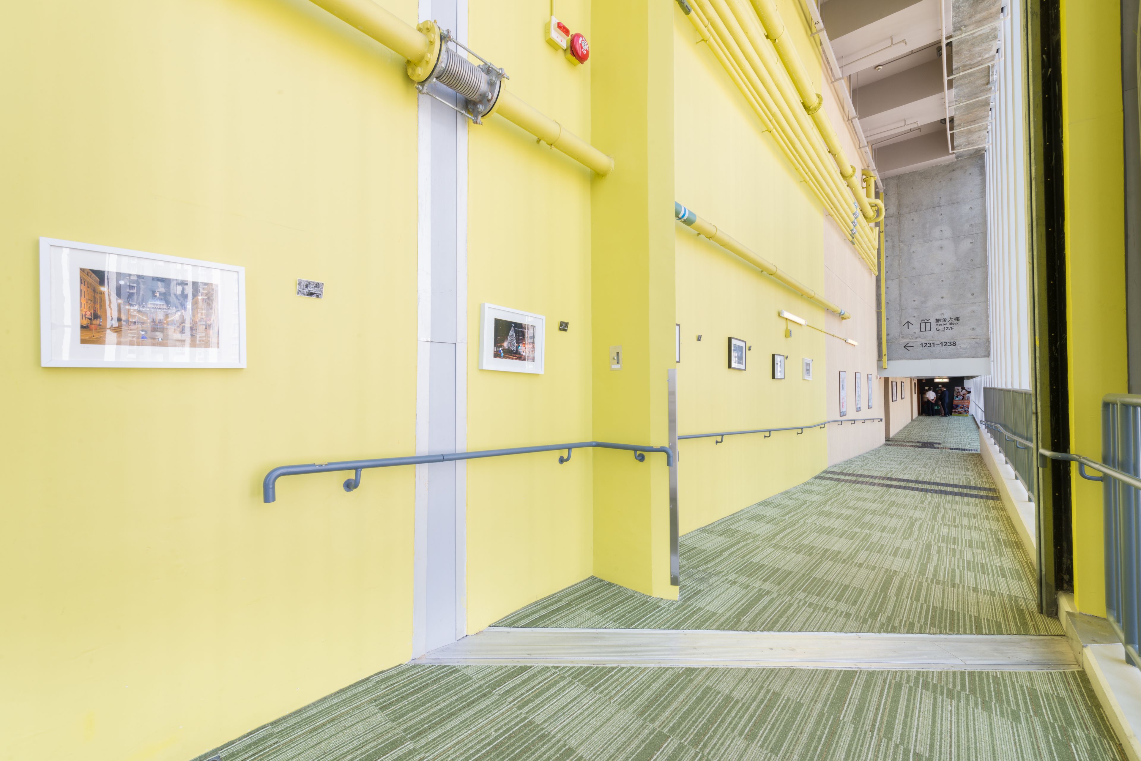 Un couloir jaune avec une moquette verte, des rampes en métal et des tableaux encadrés accrochés aux murs.