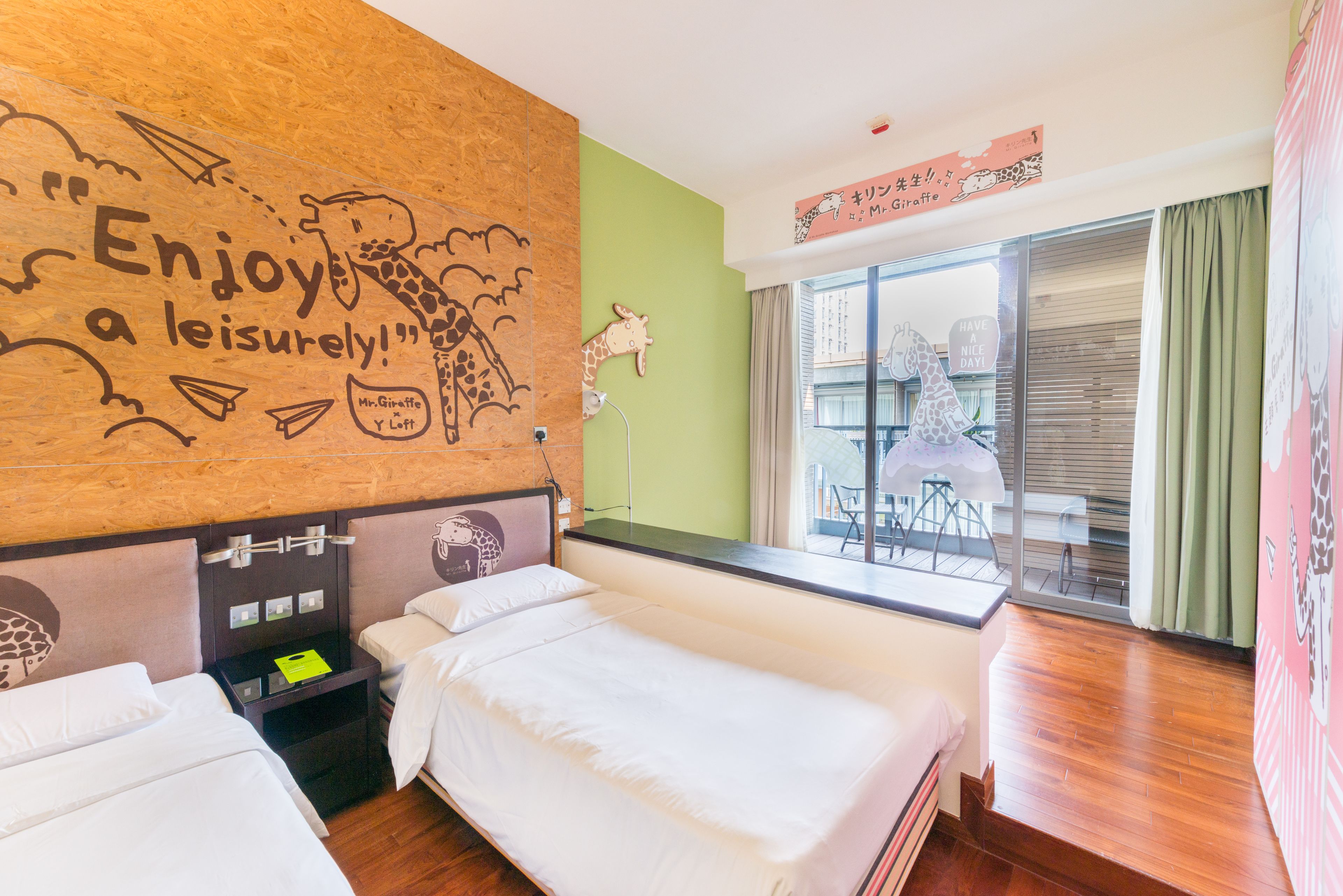 Ein Hotelzimmer mit zwei Betten, einem Holzkopfende mit Giraffenbildern, einer grünen Wand und einem Fenster mit Blick nach draußen.