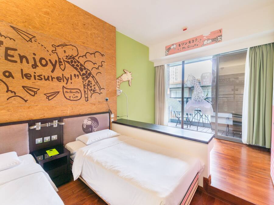 Ein Hotelzimmer mit zwei Betten, einem Holzkopfende mit Giraffenbildern, einer grünen Wand und einem Fenster mit Blick nach draußen.