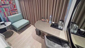 Quarto de hotel com sofá, uma mesa redonda pequena, cafeteira, lixeira e garrafa de água.
