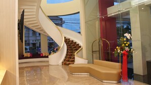 Um lobby moderno com uma escada curva, uma área de estar e um painel de vidro.
