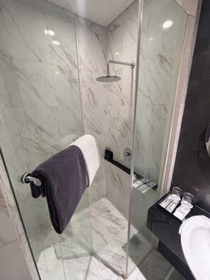 Une salle de bain moderne avec une douche à parois de verre, des carreaux de marbre, un porte-serviettes et un plan de toilette noir sur lequel sont posés des articles de toilette.