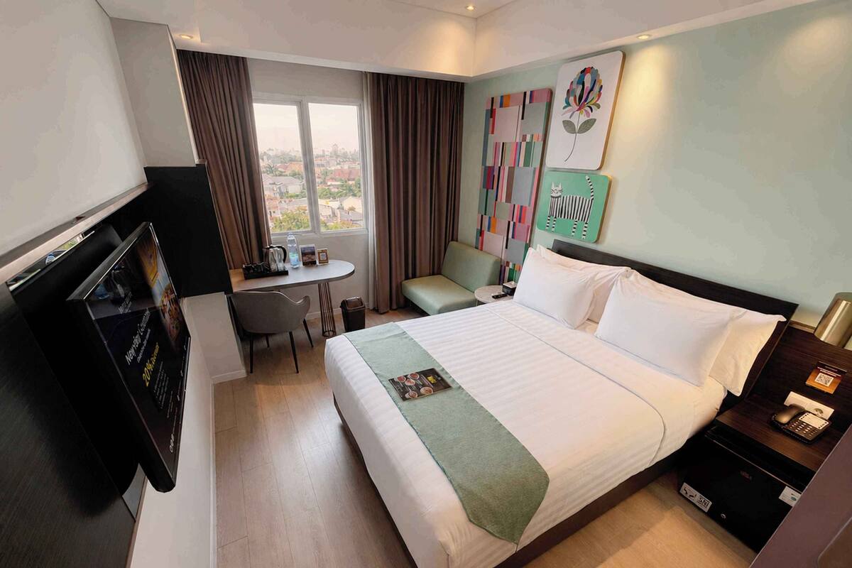 Een hotelkamer met een bed, een bureau, een stoel, een televisie en een raam met gordijnen.