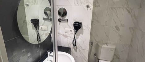 A modern bathroom with a glass shower enclosure, a round mirror, a sink, and a toilet.