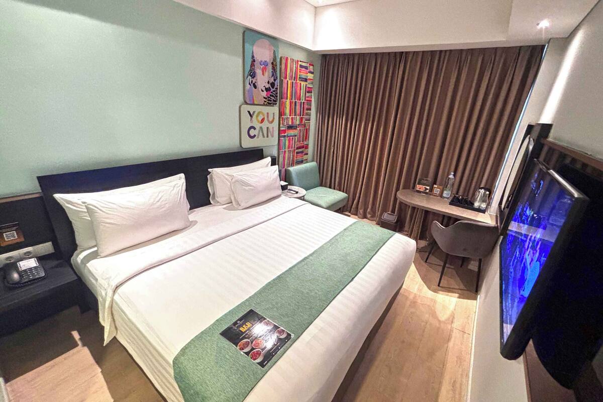 Een hotelkamer met een bed, een bureau, een stoel, een televisie en een muur met een motiverende tekst.
