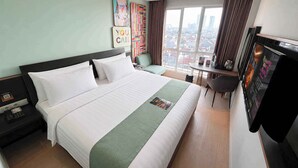 Quarto de hotel com cama grande, escrivaninha, cadeira, televisão e janela com vista para a cidade.