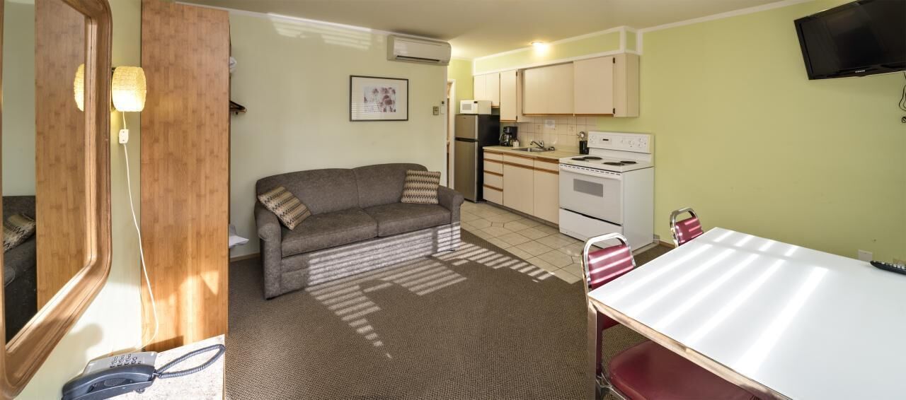 A compact living space with a sofa, a dining table, a kitchen area with appliances, and a television mounted on the wall.