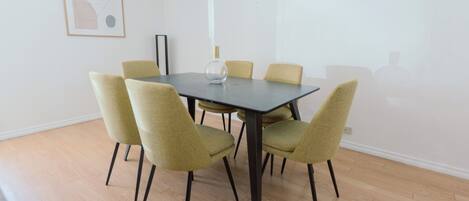 A dining area with a rectangular table surrounded by six chairs, a vase on the table, and a framed abstract artwork on the wall.