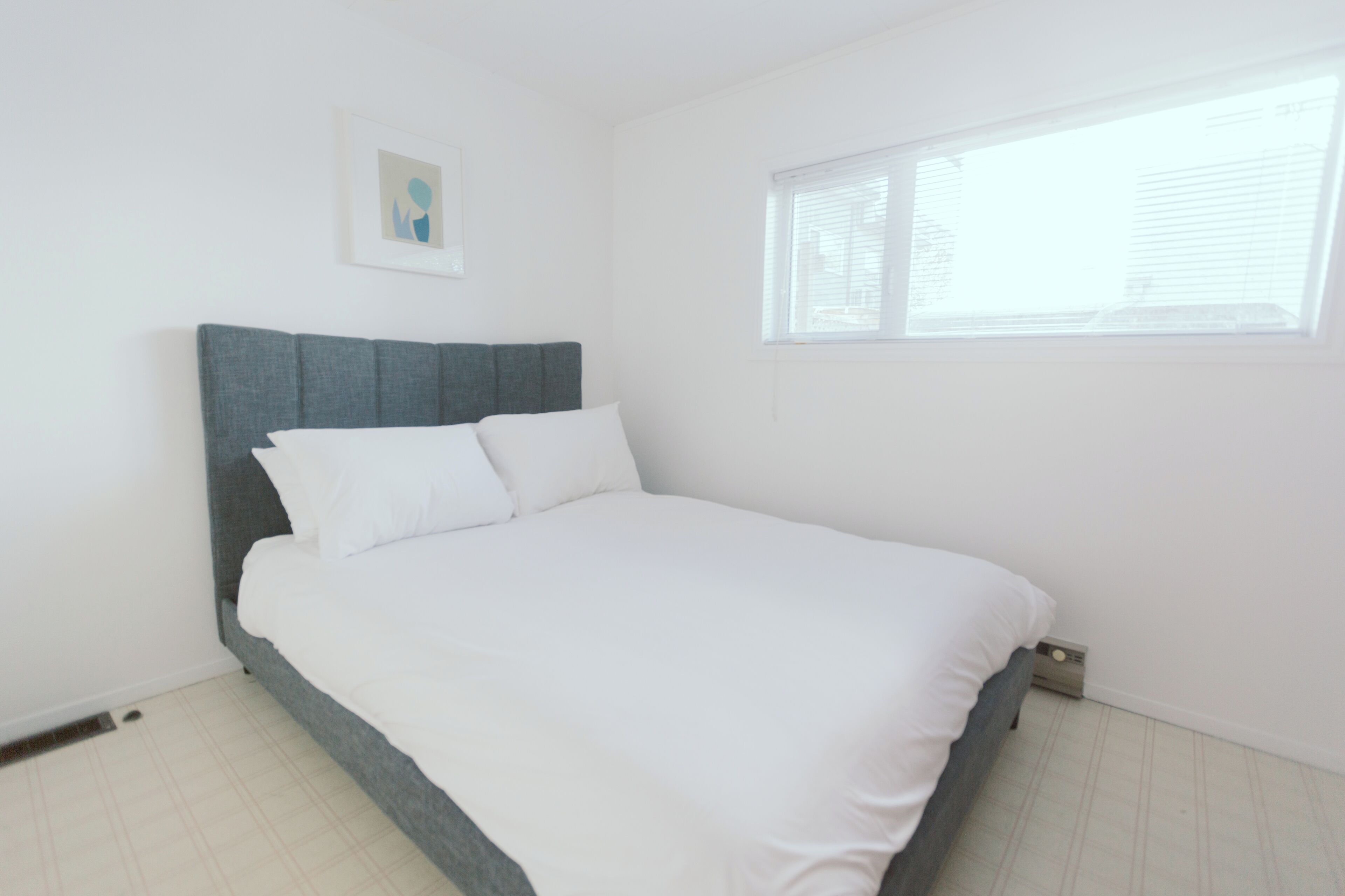 A bedroom with a bed, a window, and a picture on the wall.
