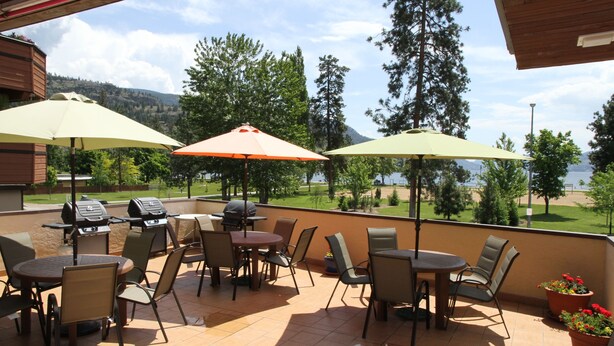 An outdoor patio with tables and chairs, umbrellas, and a grill. - Waterfront Inn (Penticton)