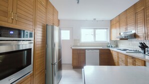 A modern kitchen with wooden cabinets, stainless steel appliances, and a large window providing natural light. - Waterfront Inn (Penticton)