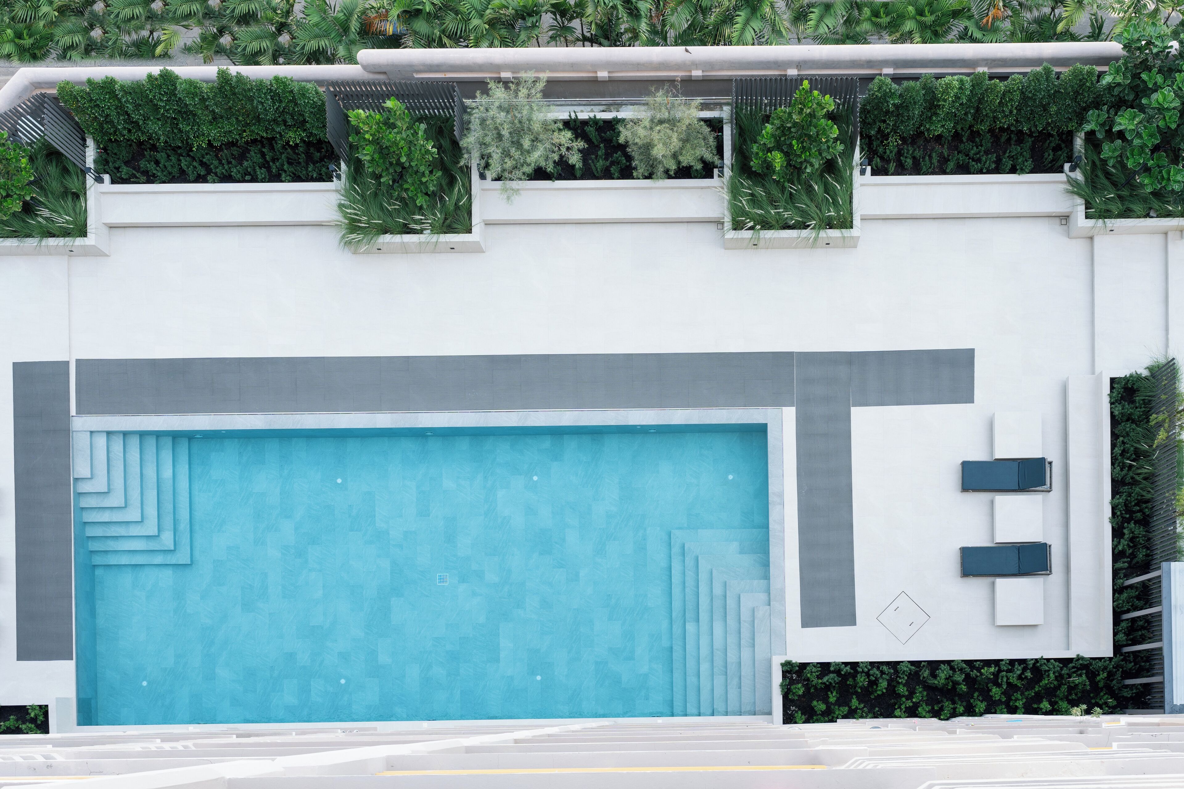 A modern building with a large blue swimming pool, a white exterior, and green plants on the roof.