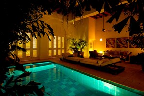 Zona junto a la piscina con una tumbona, un sofá y una planta en maceta.