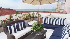 A balcony with a wicker sofa, striped cushions, a potted plant, and a large umbrella. - Hotel Casa Don Sancho by Mustique (Cartagena)