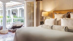 A hotel room with a large bed, a nightstand with a lamp, and a view of an outdoor patio with a chair and plants. - Hotel Casa Don Sancho by Mustique (Cartagena)
