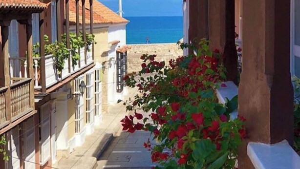 A narrow street with buildings on either side, a clear view of the sea, and blooming flowers in the foreground. - Hotel Casa Don Sancho by Mustique (Cartagena)