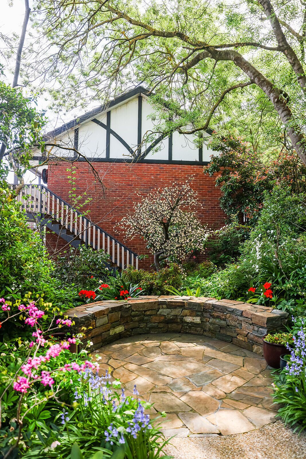 A garden with a stone bench, a brick wall, and a staircase leading to a building with a white and black facade.