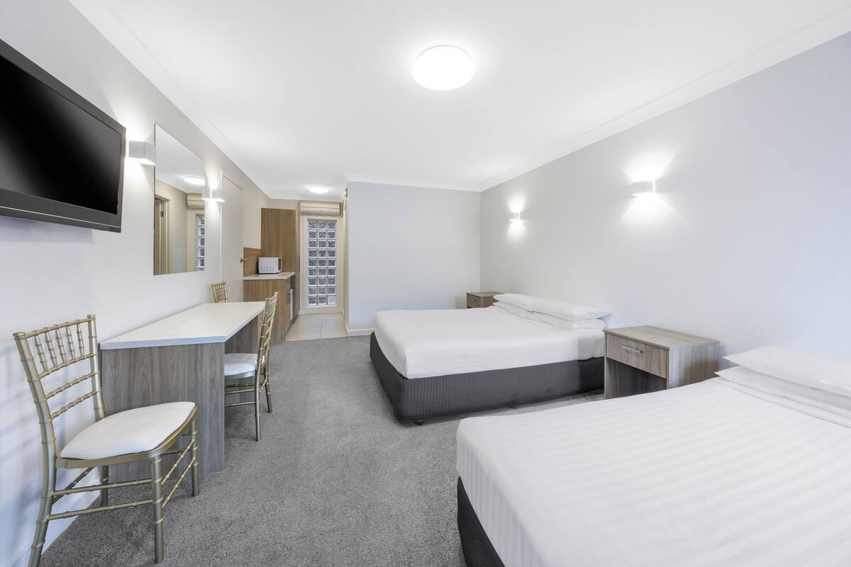 A hotel room with a desk, two beds, a TV, and a mirror.
